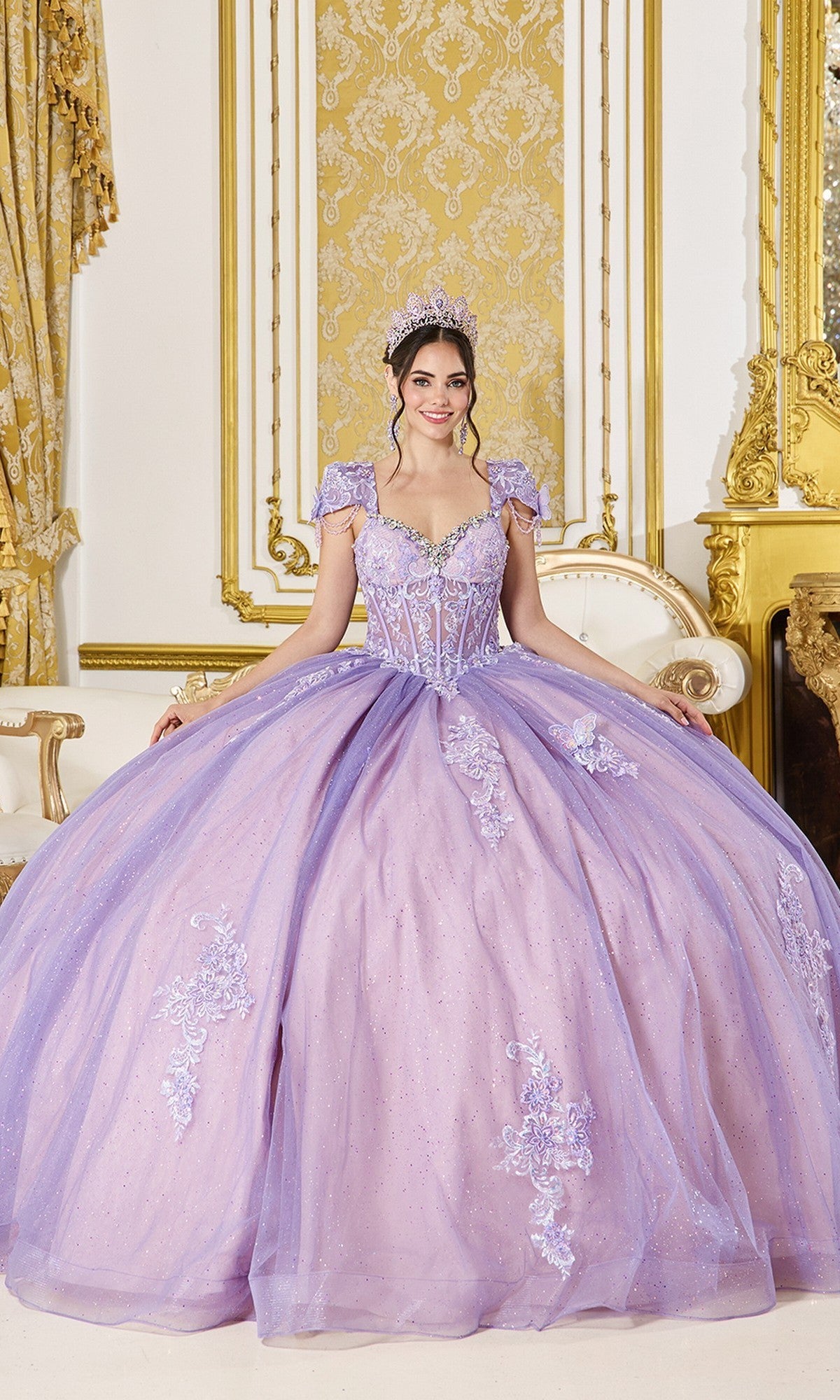 A woman in the Quinceanera Dress 5126 by Dancing Queen, featuring lilac/nude tones and floral appliqué, stands in an ornate gold and white room wearing a tiara.
